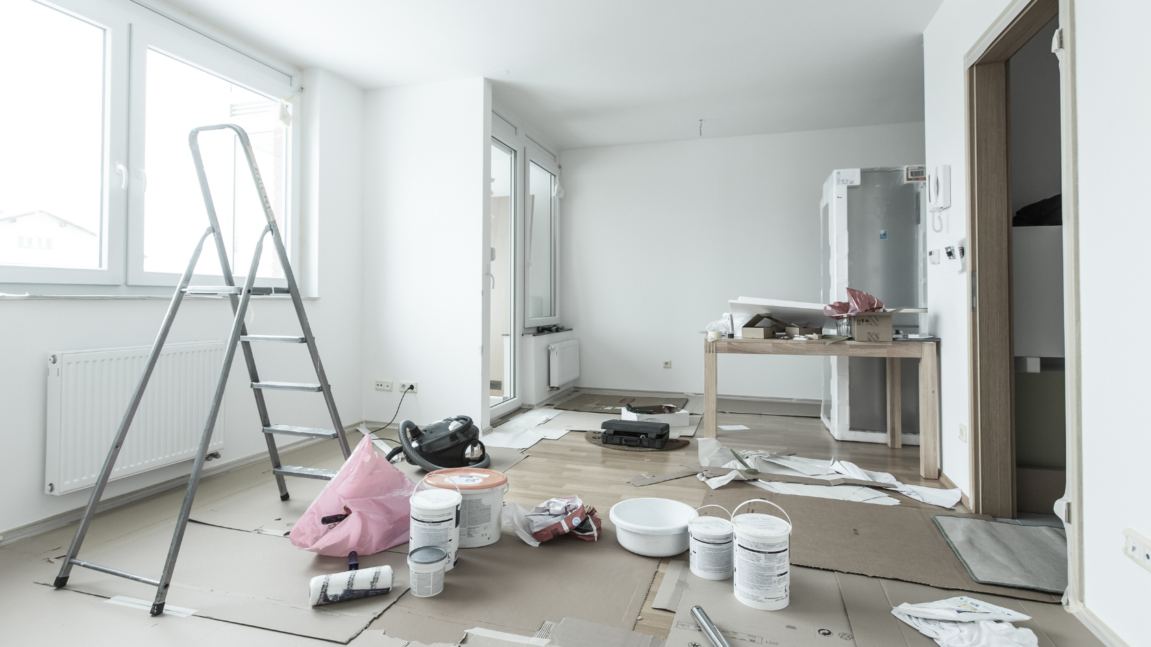 A room with a ladder, paint cans, and other items on the floor